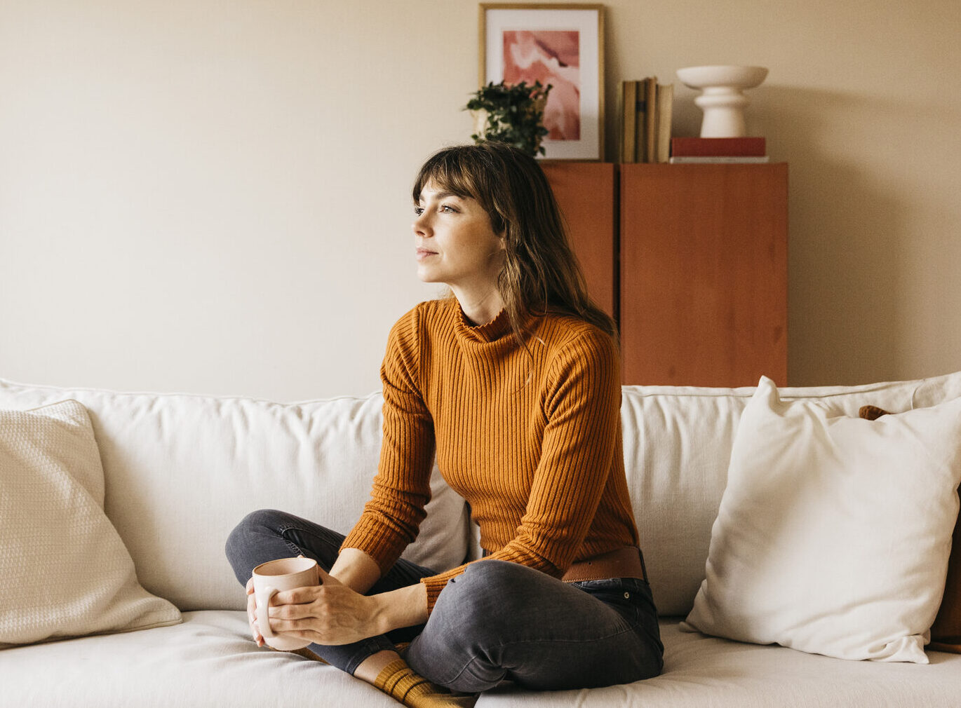 Vrouw zit met een mok op de bank in een rustige woonkamer