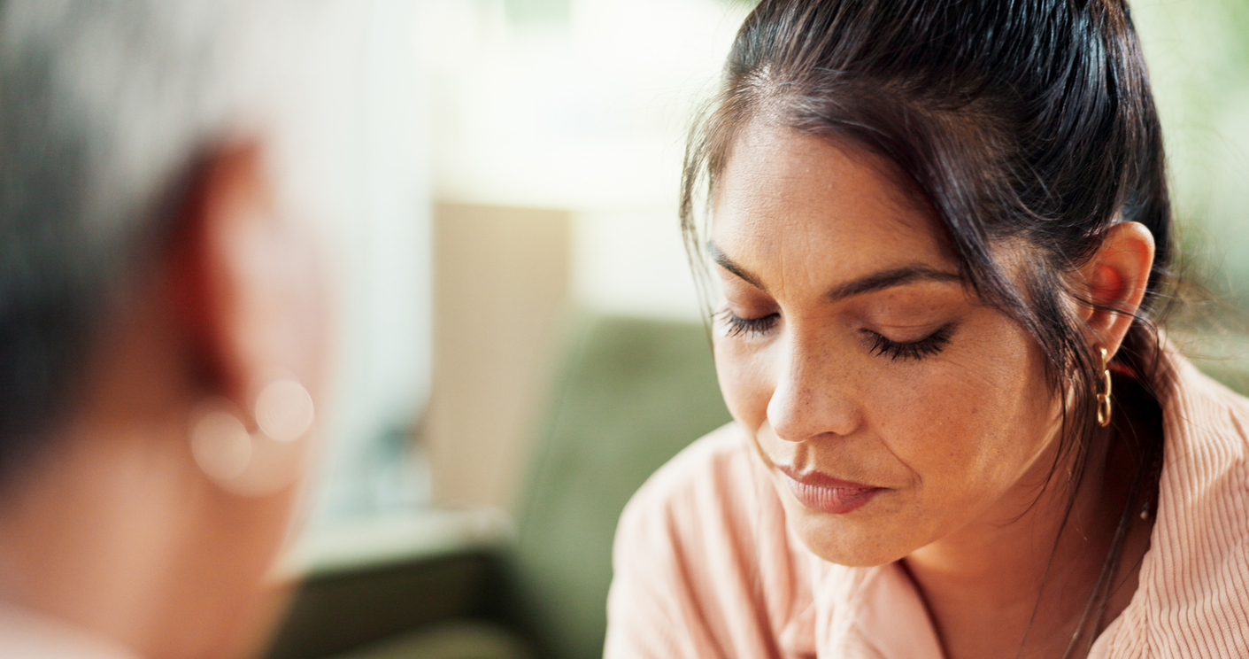 Vrouw met gesloten ogen en gebogen hoofd, tegenover een onscherp afgebeelde persoon.