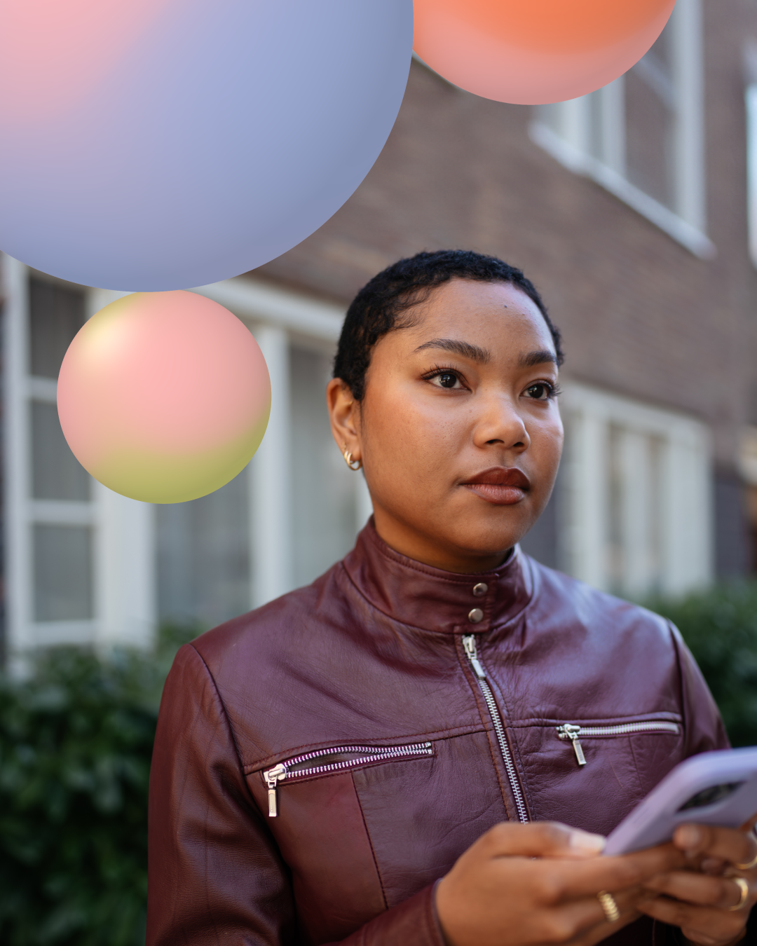 Jonge vrouw met kort haar in een bruine jas, met gekleurde ballonnen op de achtergrond.